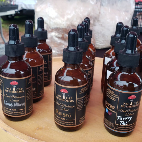 Row of No Cap Mushrooms tincture bottles on a wooden surface with a blurred outdoor background.